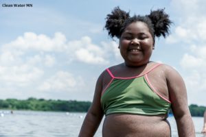 Image of a smiling girl wearing a swimsuit with a lake in the background