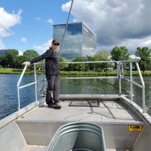 A woman stands in the front of a boat; attached to the front are wires which send electric currents into the water.