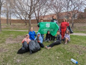 A group of kids hold a 4H banner, posing with a few bags of trash they pulled out of the creek.