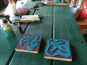 Wooden block prints sit on a table with paint equipment nearby. ONe block features a stylized Ojibwe man and the second block features a stylized turtle.