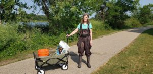 Image of a woman wearing waders with a cart filled with buckets and bags of corn