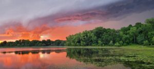 Bush lake reflecting colorful storm clouds at sunset.