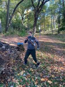 A person holds a rake against a forest background with fall leaves