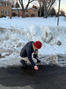 A person scoops meltwater into a cup with a large pile of snow in the background.